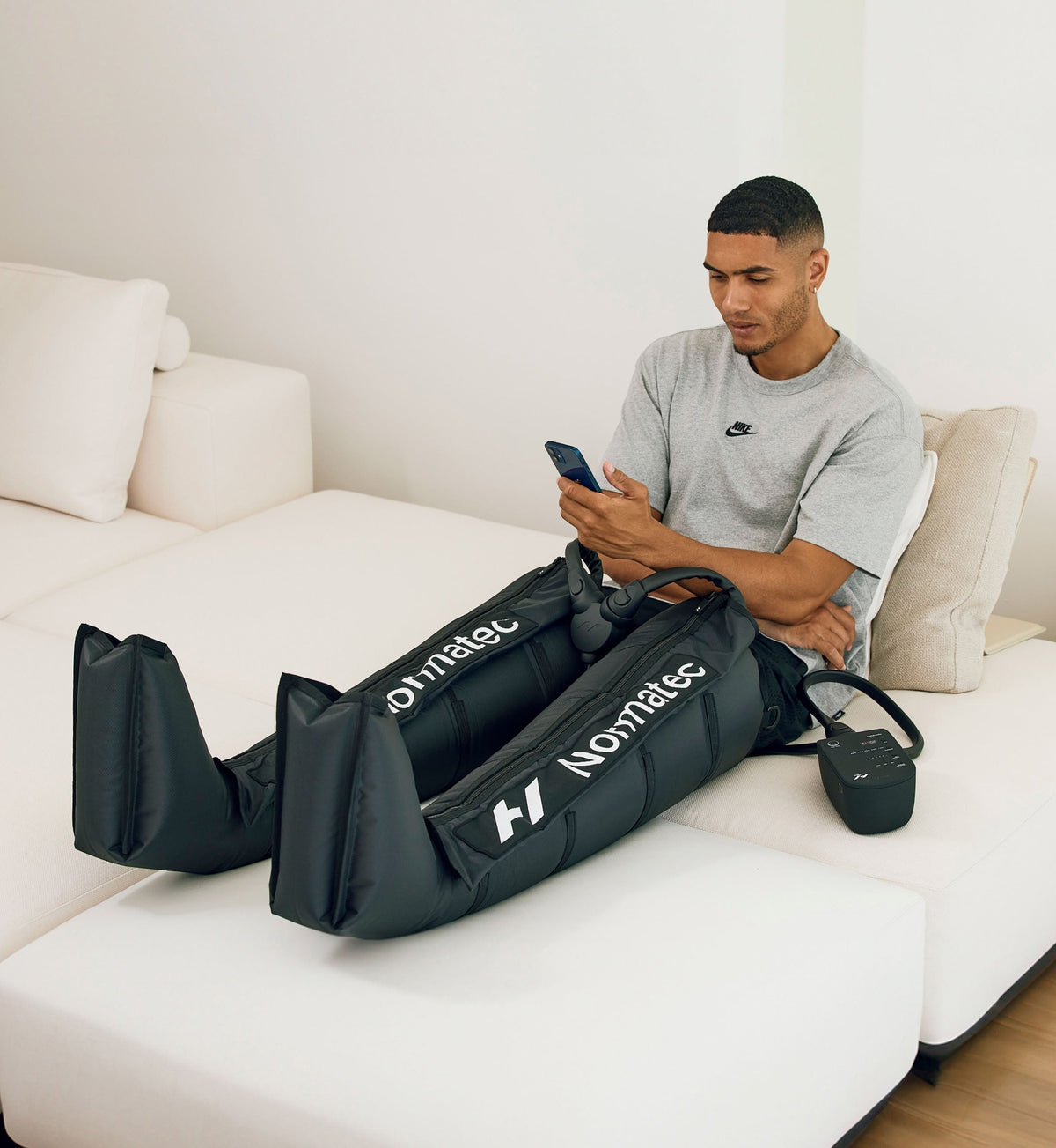 Mand sidder i en sofa med sin telefon og har Normatec 3 Legs på benene